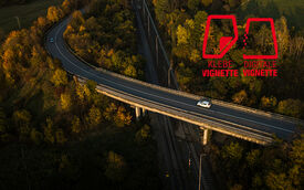 0454_21 Digital_740x462_vignette.jpg Weißes Auto auf einer Autobahnbrücke. Rechts im Bild die Symbole für die Klebe-Vignette und Digitale Vignette in Österreich.