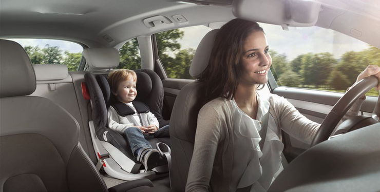 Kindersicherung im Auto © ÖAMTC Eine Frau sitzt am Fahrersitz und fährt lächelnd ein Auto. Auf der Rückbank ist ein Kleinkind im Kindersitz.