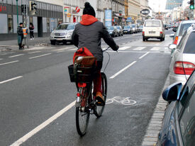 Radfahrer auf Mehrzweckstreifen Ein Radfahrer fährt auf einem Radfahr-Mehrzweckstreifen rechts auf einer Straße. Der Mehrzweckstreifen ist durch eine weiße Sperrlinie abgegrenzt und einem Fahrradsymbol am Boden gekennzeichnet.