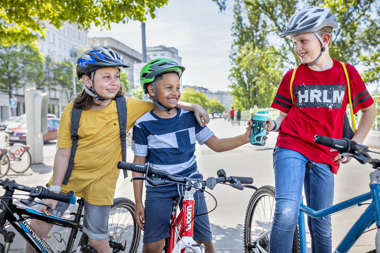 © ÖAMTC Drei Kinder machen im Sommer auf ihren Fahrrädern auf einer Straße Halt.